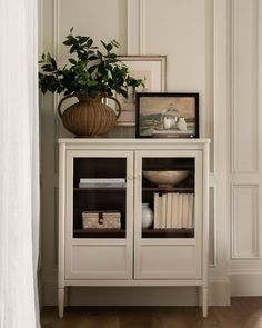 a white cabinet with some books and a potted plant