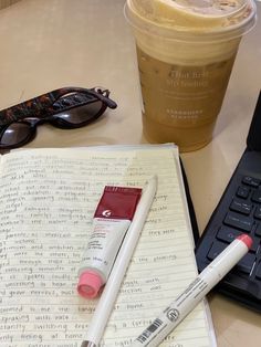 an open notebook with two markers and a cup of coffee next to it