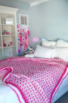 a bed with white sheets and pink bedspread in front of a bookcase