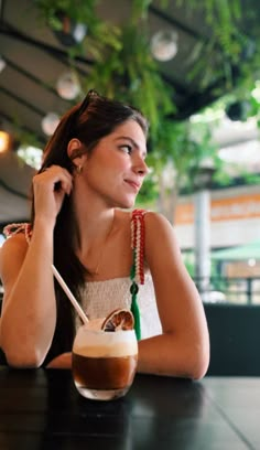 a woman sitting at a table with a drink in her hand and looking off to the side