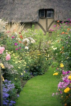 a garden filled with lots of flowers next to a grass covered building and a window