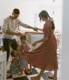 a woman in a red dress is dancing with two children and an adult standing next to her