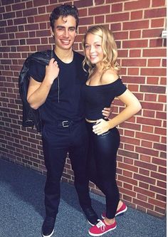 a man and woman standing next to each other in front of a brick wall smiling