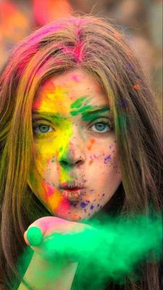 a woman with colorful paint on her face and hands holding a green substance in front of her face