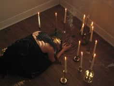 a woman is laying on the floor in front of many candles with her head down