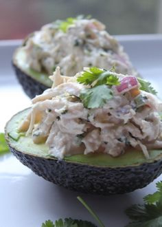 an avocado filled with tuna salad on top of green garnish and cilantro