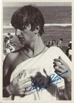 an old photo of a man in a towel on the beach with people behind him