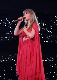 a woman in a red dress holding a microphone and singing into a microphone with lights behind her