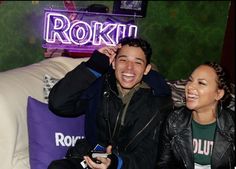 two people sitting next to each other in front of a neon sign that reads rokin