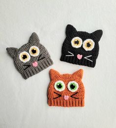 three crocheted hats with cats on them, one has green eyes and the other is orange