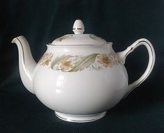 a white tea pot with flowers painted on the top and bottom, sitting on a black background