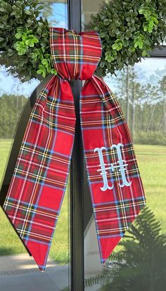 a wreath with a mono on it and a red plaid bow hanging from the front door