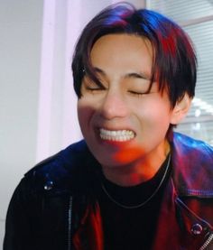 a man with his eyes closed smiling and wearing a black shirt, leather jacket and necklace