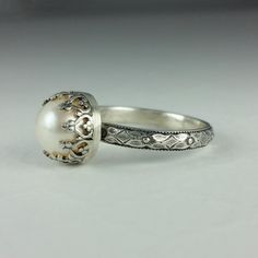 Timeless and classic, this vintage inspired pearl engagement ring is reminiscent of the Edwardian era when fine metalwork was designed with intricate details and delicate settings fashioned to resemble patterns in fine lace. Handcrafted from recycled sterling silver, a lightly oxidized floral band is set with a luminous 8-8.5mm cultured creamy white freshwater pearl in a filigree heart-wire crown setting that is hand-patinaed and polished to a soft shine. Pearl engagement rings are not only uniq Elegant Wedding Jewelry With Milgrain Detail, Elegant White Engraved Rings, Classic Pearl Ring For Wedding, White Sterling Silver Engraved Wedding Ring, Classic Wedding Pearl Ring, Timeless Oval Pearl Ring For Wedding, Elegant White Filigree Ring With Intricate Design, Elegant Milgrain Jewelry For Wedding, Elegant White Gold Pearl Ring With Rose Cut Diamonds