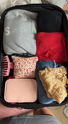 an open suitcase filled with clothes on top of a bed next to a person's legs