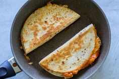 two quesadillas in a frying pan on the stove top, one cut in half