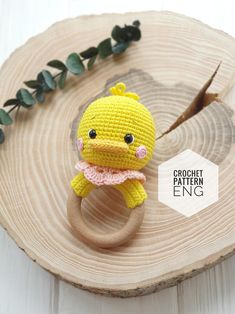 a crocheted yellow bird ring sitting on top of a piece of wood next to green leaves