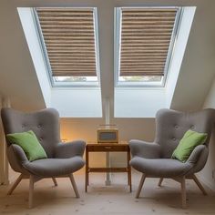 two gray chairs with green pillows in an attic room under a skylight and a small table