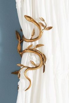 the curtain is hanging on the wall with gold metal leaves and branches attached to it