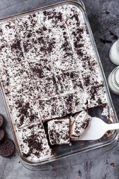 a pan filled with chocolate cake and oreo cookies next to two cups of milk