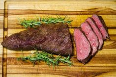 sliced steak on a cutting board with rosemary garnish and seasoning sprig