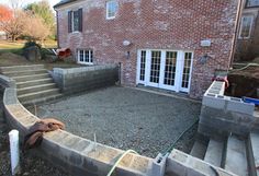 a brick house with steps leading up to the front door and patio area, surrounded by gravel