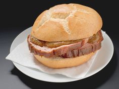 a roast beef sandwich on a white plate with a napkin under it and black background