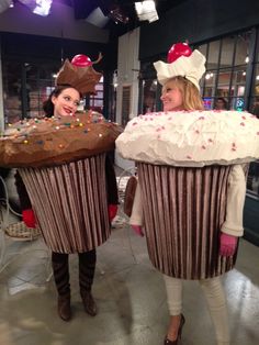 two women dressed in costumes holding giant cupcakes