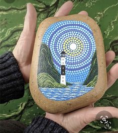 a hand holding a rock with a lighthouse painted on it