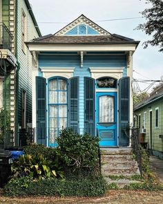 a blue and white house with shutters on the front door is next to some bushes