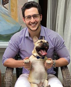 a man sitting in a chair holding a small dog with its mouth open and tongue out