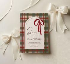 a plaid wedding card with a red bow and ribbon on the front, sitting next to some white ribbons