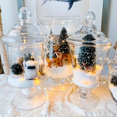 a table topped with glass jars filled with snow covered trees and reindeer figurines