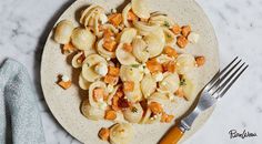 a white plate topped with pasta and vegetables next to a silver fork on top of a marble counter