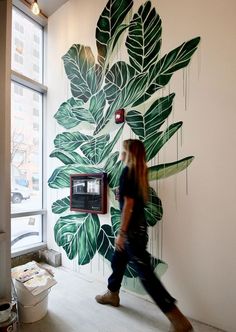 a woman walking past a painting on the side of a wall in an office building