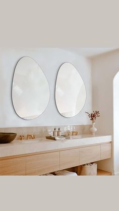 there are two mirrors on the wall above the sinks in this bathroom, one is oval