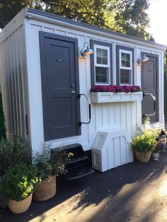 a white and gray shed with potted plants on the outside, next to it