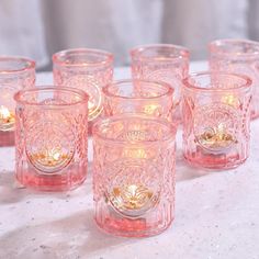 pink glass tumblers lined up on top of a white table with candles in them