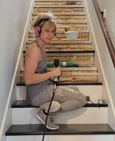 a woman with headphones sitting on the stairs while holding a microphone and listening to music