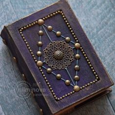 an old book with beaded decorations on the front and back cover sitting on a wooden table