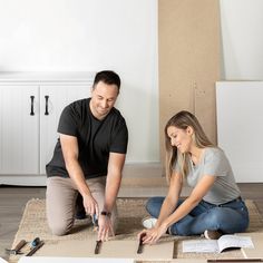 a man and woman sitting on the floor in front of a cardboard box with tools