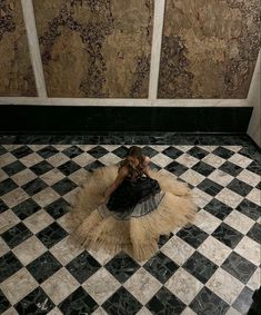 a woman sitting on top of a black and white checkered floor next to a wall