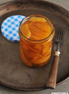 a glass jar filled with pickled apples on top of a plate next to a fork