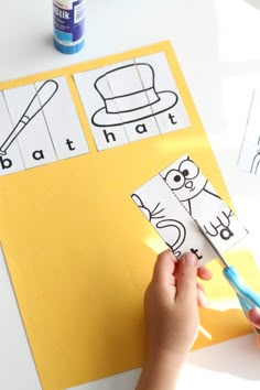 a person cutting out paper with scissors on top of a white table next to a yellow envelope