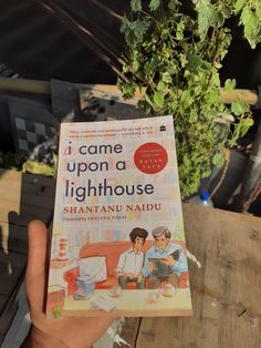 the book i came upon a lighthouse by shantanu naddu is held up in front of a tree