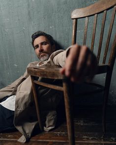 a man sitting in a wooden chair with his hand on the back of the chair