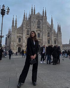 a woman standing in front of a large cathedral with lots of people around her looking up at the sky