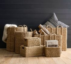 several baskets are stacked on the floor next to a pillow and throw pillows in front of a black wall