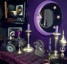 a table topped with candles next to a mirror and other items in front of a purple wall