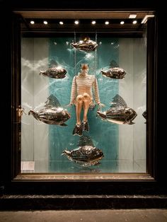 a mannequin sitting in front of a display case filled with silver fish and other metal objects